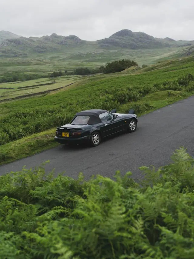 A classic Mazda car parked on a scenic road, reflecting on Mazda car history and design evolution